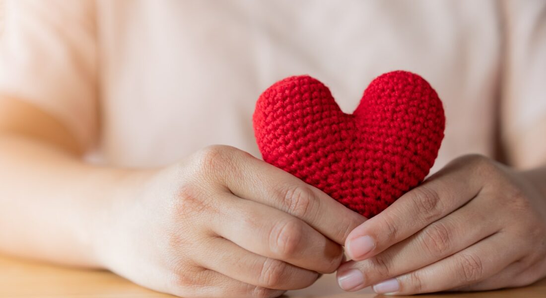 Adult hands holding a yarn red heart