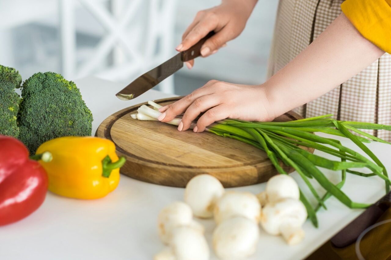 cropped image of woman cutting green onion on cutting board